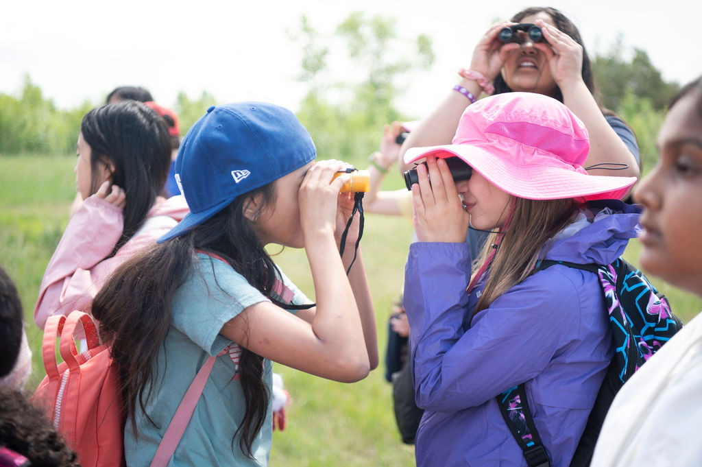 Two young girls looking at each other through binoculars